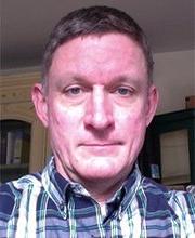 headshot photo of professor Andrew Armstrong with short greyish brown hair wearing a blue, white and green plaid button down shirt with collar