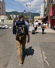 科林斯慕斯 walking down a street away from the camera with a large back pack on and mountains in the distance