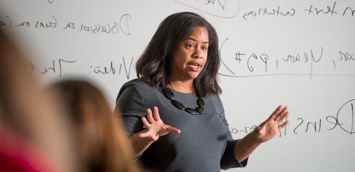 A professor teaching class in front of a white board with notes including "Discussion on guns" and "text citations."