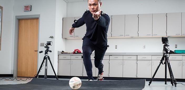 a student in the biomechanics lab wearing all black with little velcro white balls attached to his clothes bowling on a mat with cameras around him